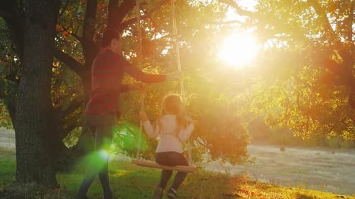 Woman Pushing Child on Swing at Sunset