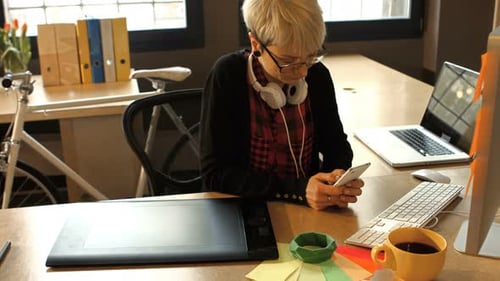 Woman Looking at Phone at Modern Graphic Design Desk