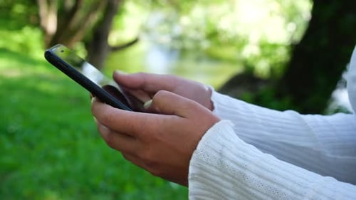 Close Up Woman Hands Uses the Phone on the Background of the Park