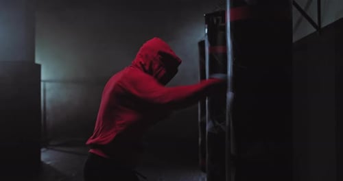 Silhouette eines männlichen Boxers mit Kapuze, ein Kämpfer schlägt einen Boxsack