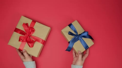 Hands Holding Wrapped Gifts on Red Background