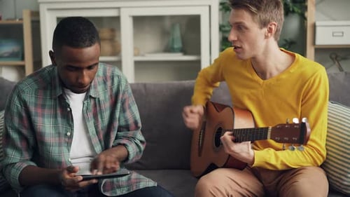 Two Friends Play Guitar and Tablet Indoors