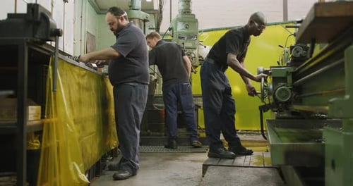 Caucasian and African American male factory worker standing at a workbench and operating machinery