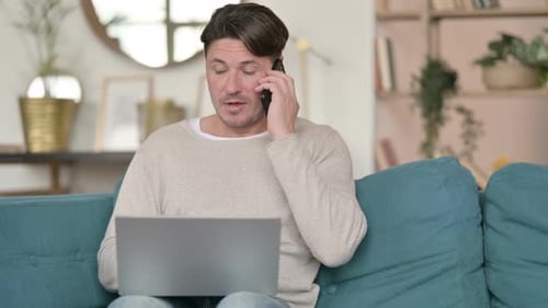 Man Talking on Phone with Laptop on Lap