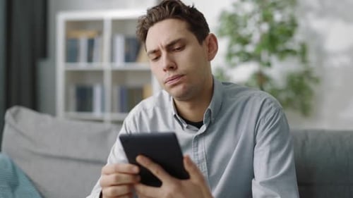 Stressed Man Using Tablet Inside Home on Couch
