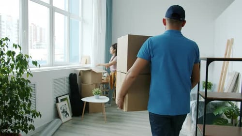 Man Carries Boxes into Apartment while Woman Unpacks