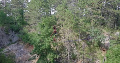 Un hombre trata de mantener el equilibrio mientras está holgazaneado en una cuerda floja en las montañas.