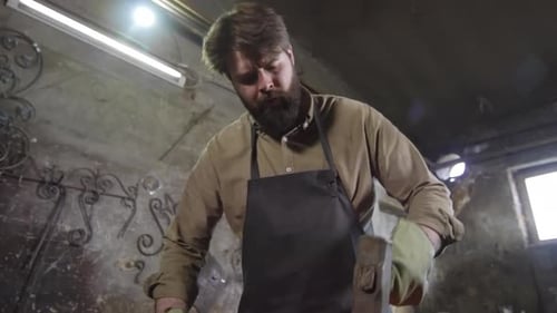Bearded Blacksmith Hitting Hot Metal With Hammer