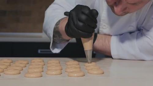 Ein kaukasischer Konditor beugt sich über den Tisch und legt Makronenteig aus einem Gebäckbeutel