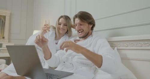 Excited Couple Looks at Laptop in Hotel Robes