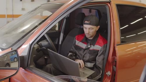 Mechanic Sitting in Car and Doing Diagnostics with Laptop