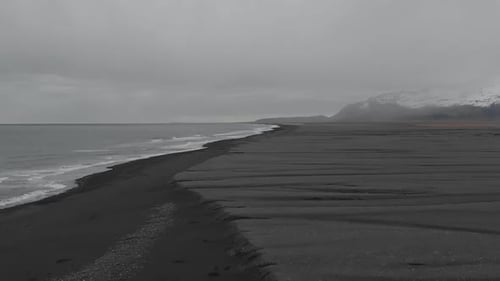 Establishing shot flying along the vast landscape of black sand beach.