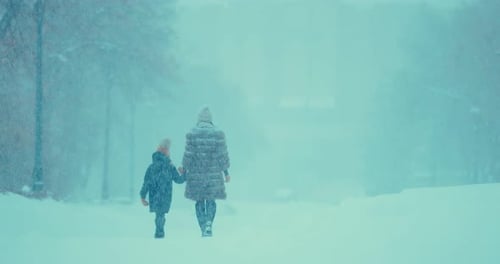 Woman with a Girl Go Down the Snow-covered Road. Mom and Daughter Are Walking in the Park