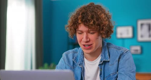 Young Adult with Curly Hair Uses Laptop Indoors