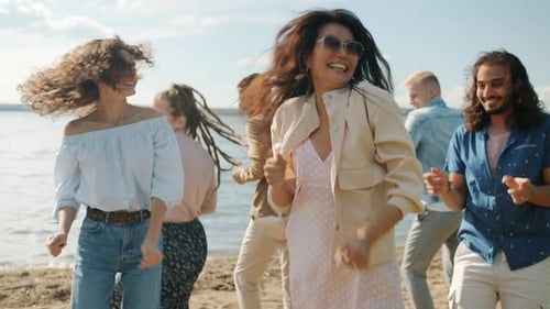 Ralenti de filles et de garçons qui dansent, sautent et s'amusent sur la plage un jour d'été