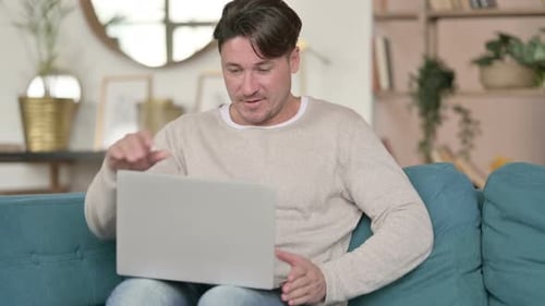 Man Opens Laptop Sitting on Couch Indoors