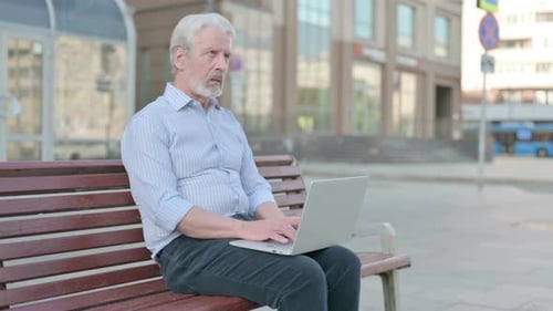 Senior Man Using Laptop on Bench Outdoors