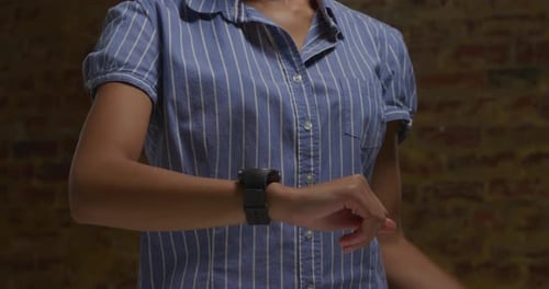 Woman Interacts With Smartwatch Against Brick Wall