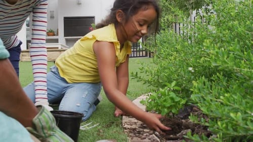 Hispanic girl with parents learning planting flowers in the garden