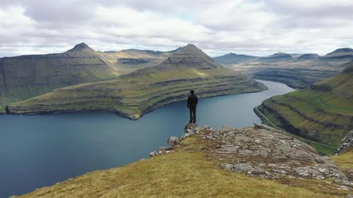 Flying Around a Hiker at the Top of a Mountain Above Funningur on Faroe Islands