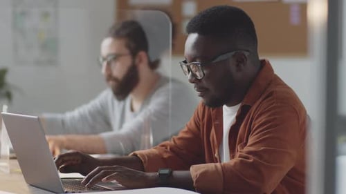Homme noir travaillant sur un ordinateur portable au bureau avec mur de protection en verre