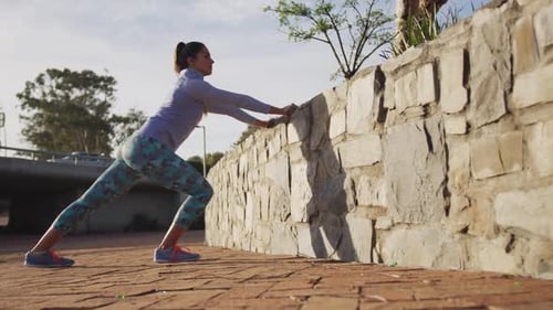 Woman Stretching Against Wall in Urban Park