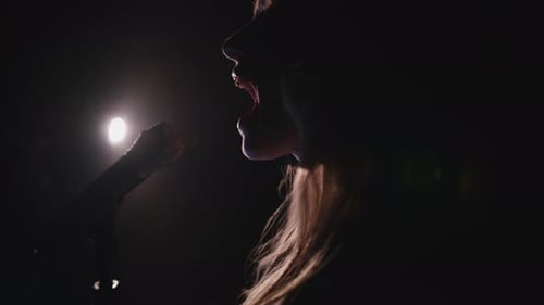 Close-up of the Face of the Singer with Microphone on a Black Smoky Background. The Singer Sings a