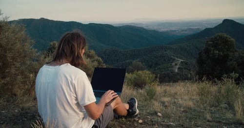 Freelance Worker Type Using Notebook Computer Sitting on Top of Mountain