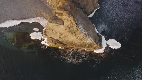 Les vagues frappent le rocher côtier, qui est entouré de glace