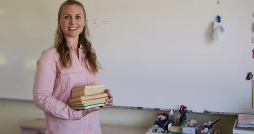 Female teacher holding stack of books in school