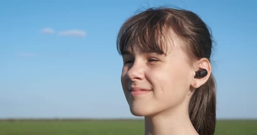 Girl Taps Wireless Earbuds Smiling Outdoors