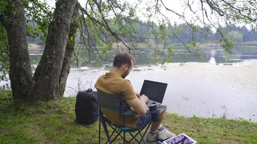 Man Works on Laptop by Lake in Nature