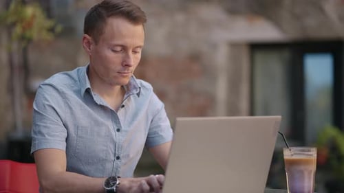 Handsome Freelancer Businessman in Glasses Diligently Working on Laptop in Cafe