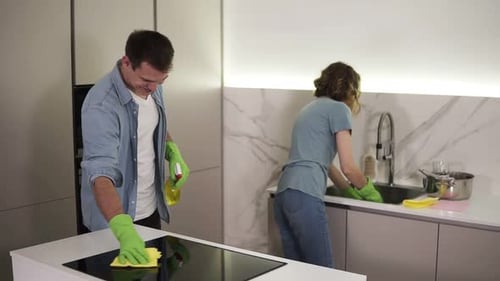 Young Smiling Married Couple in Casual Clothing and Both in Green Gloves Cleaning Kitchen After