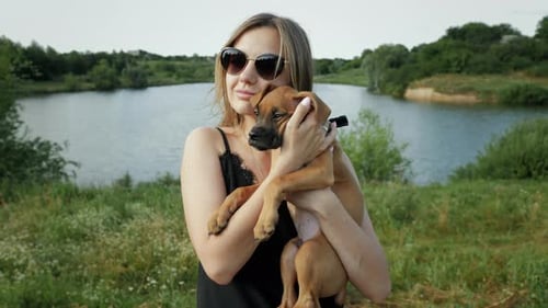 Young Woman Holding Puppy in Rural Lakeside Setting