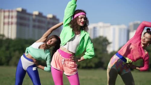 Energetic Women Stretch in 80s Outfits Outdoors