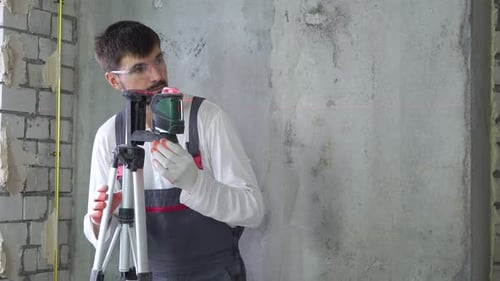 Builder Doing Measures with Laser Level at Construction Site