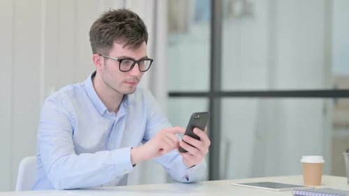 Attraktiver junger Mann nutzt Smartphone im Büro