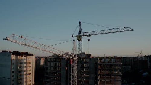 Vista aérea desde Zumbido de grúas de construcción a la luz del atardecer. Edificio de obra en construcción en la ciudad