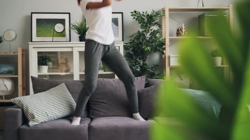 Woman with Headphones Dancing on a Gray Couch