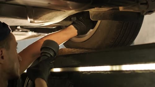 Mechanic Repairs Car Wheel with Power Tool