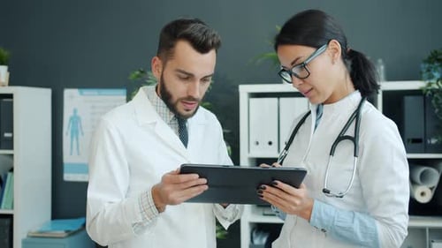 Medics in White Gowns Using Tablet at Work Talking Using Gadget in Office