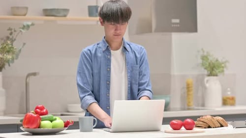 Young Adult Typing on Laptop in Kitchen