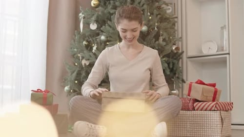 Woman opening Christmas gift box by tree