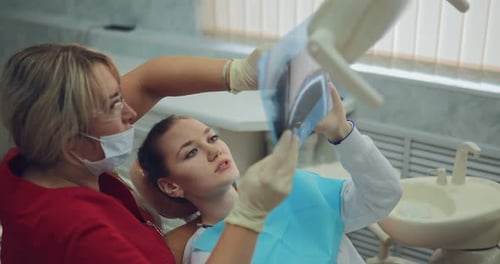 Hübsche Zahnärztin schaut sich das Röntgenbild der Patientin an und erklärt, wie die Zähne behandelt werden