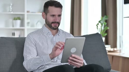 Man Celebrates Good News Using Tablet on Sofa