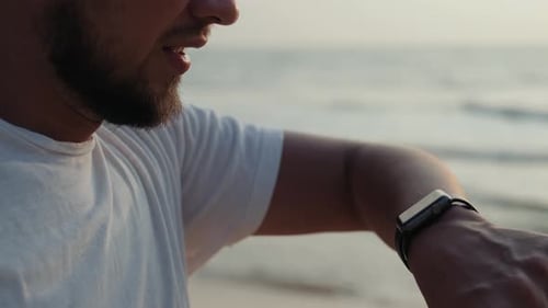 Man Checks Smart Watch at Sunrise on Beach
