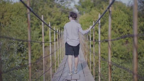 Guy Walks on Suspended Bridge in the Forest