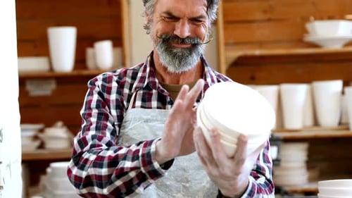 Potter Inspecting Ceramic Plates in Pottery Workshop