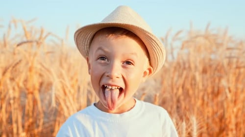 Baby Boy Stands in Straw Hat in Field Against Background of Harvest of Golden Wheat Spikelets and